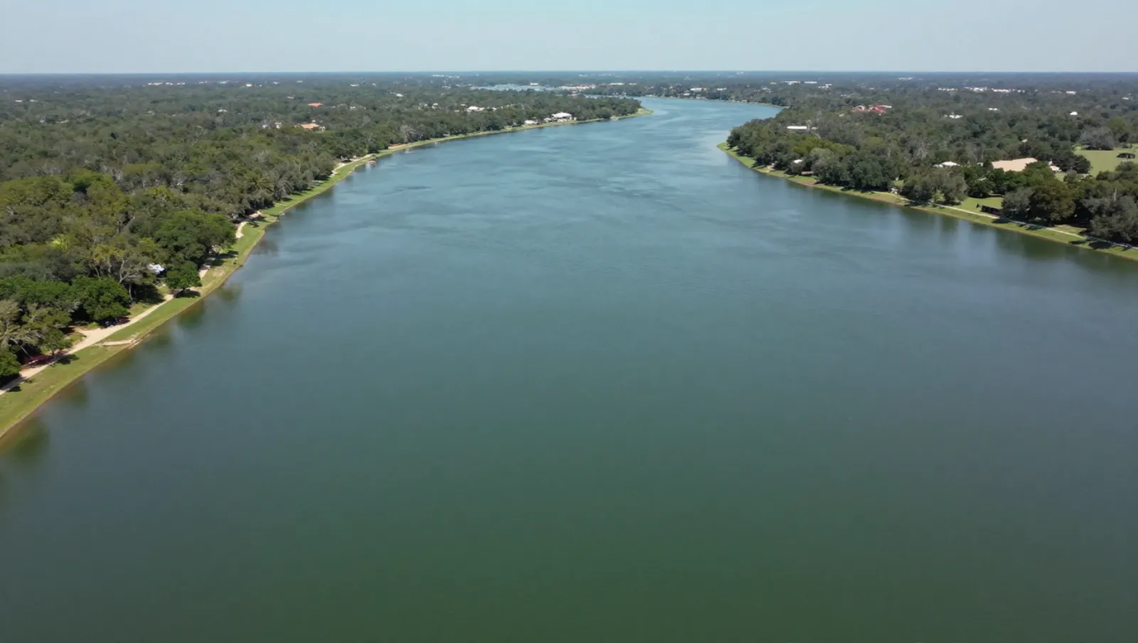 A wide river flows through flat, tree-lined terrain with scattered homes; no machinery or active work is visible — Daniel Dean Land Clearing, Southeast Texas