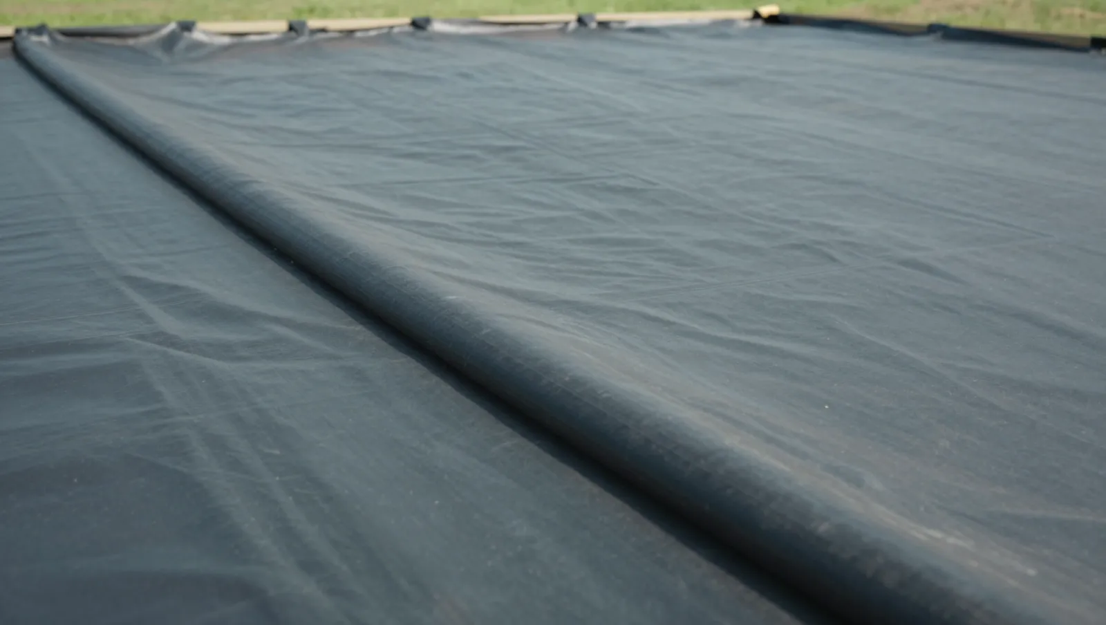 Black agricultural tarp laid over flat grassland terrain with no machinery visible during soil covering work — Daniel Dean Land Clearing, Southeast Texas