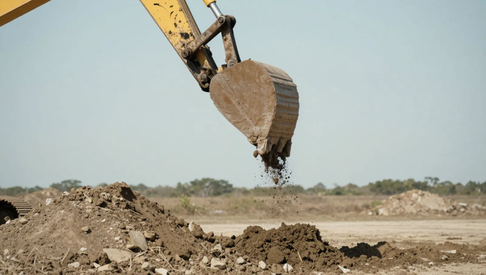 How Dredging Services Improve Drainage on Agricultural Land Yellow excavator dumps soil onto dirt piles at a rocky construction site — Daniel Dean Land Clearing, Southeast Texas