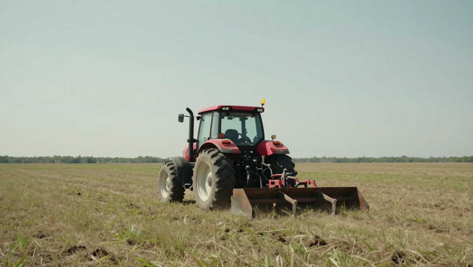 A red tractor plows a dry grassy field on an open plain — Daniel Dean Land Clearing, Southeast Texas