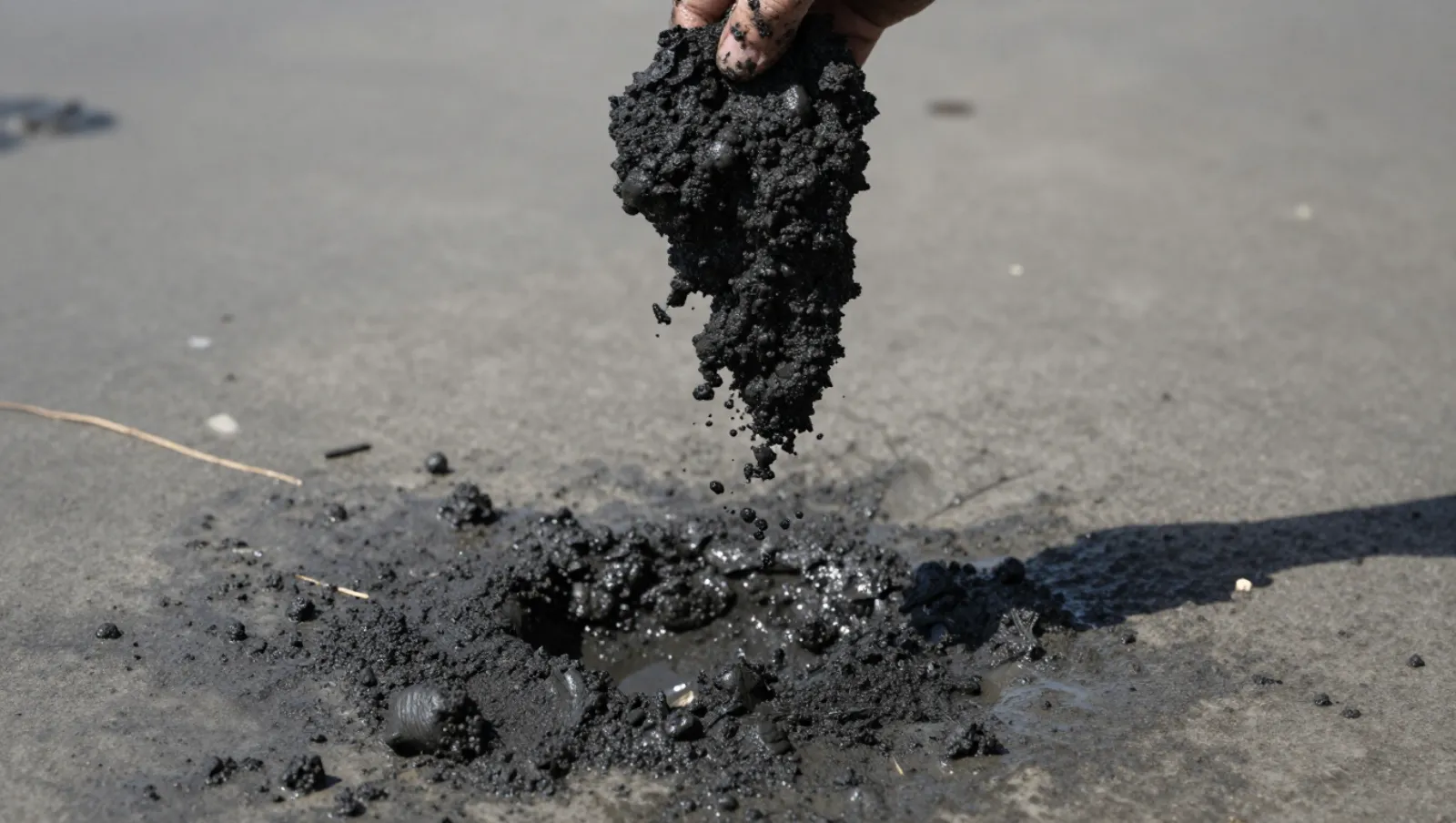 Hand gathers dark viscous material from an asphalt road; no machinery visible, work involves collecting the sludge — Daniel Dean Land Clearing, Southeast Texas