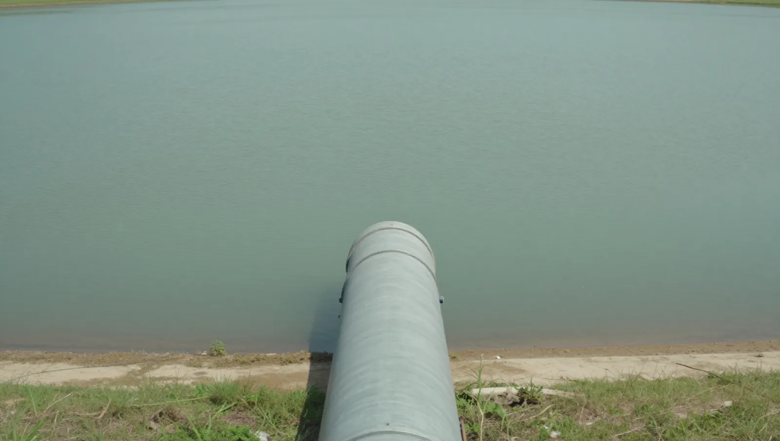 Pond Excavation Cost: Ways to Save Without Cutting Quality Metal pipeline on grassy terrain pumps liquid into calm waters — Daniel Dean Land Clearing, Southeast Texas