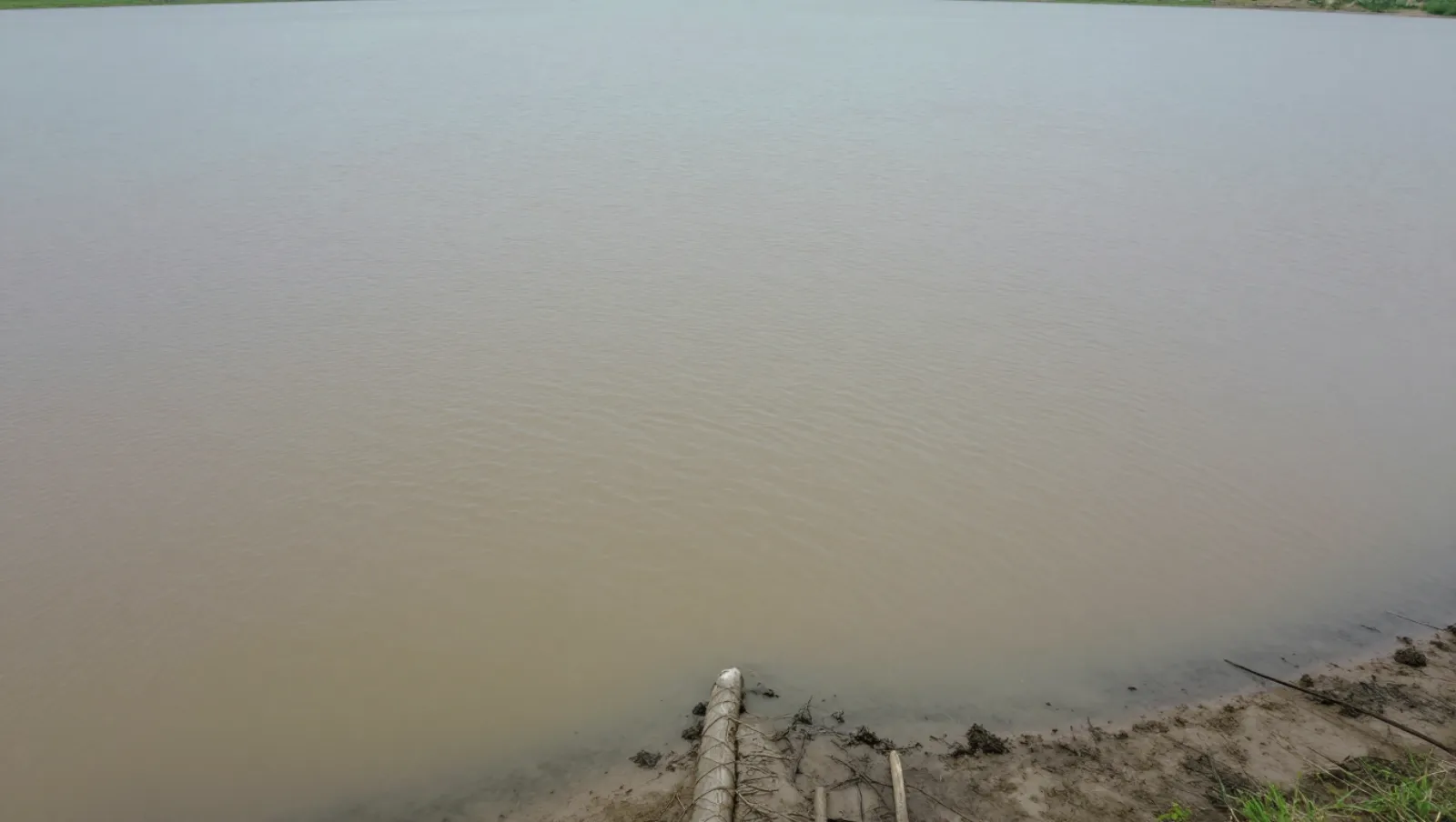 Pond Sludge Remover: Why Pond Smells and How to Fix It Fast Muddy riverbank terrain has vertical pipe machinery for pipeline installation near water — Daniel Dean Land Clearing, Southeast Texas