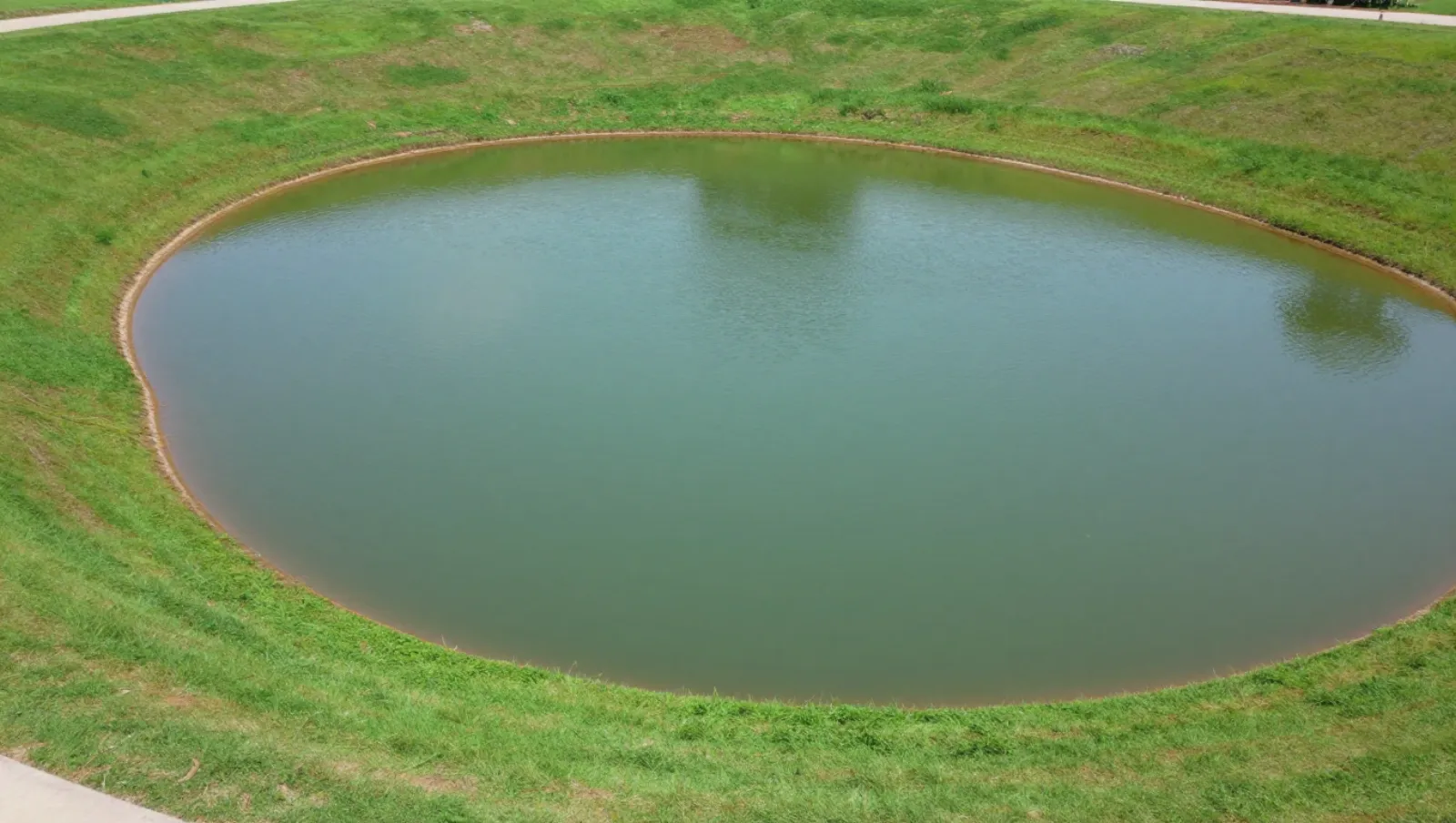 No machinery in grassy terrain with circular water body shows completed landscaping work — Daniel Dean Land Clearing, Southeast Texas