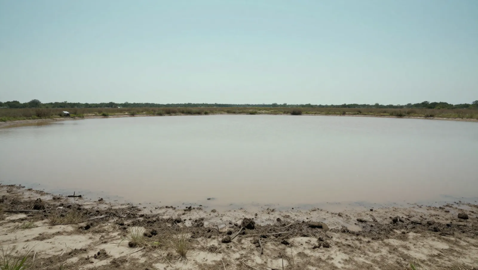 Muddy shoreline terrain borders murky water; no machinery or active work visible — Daniel Dean Land Clearing, Southeast Texas