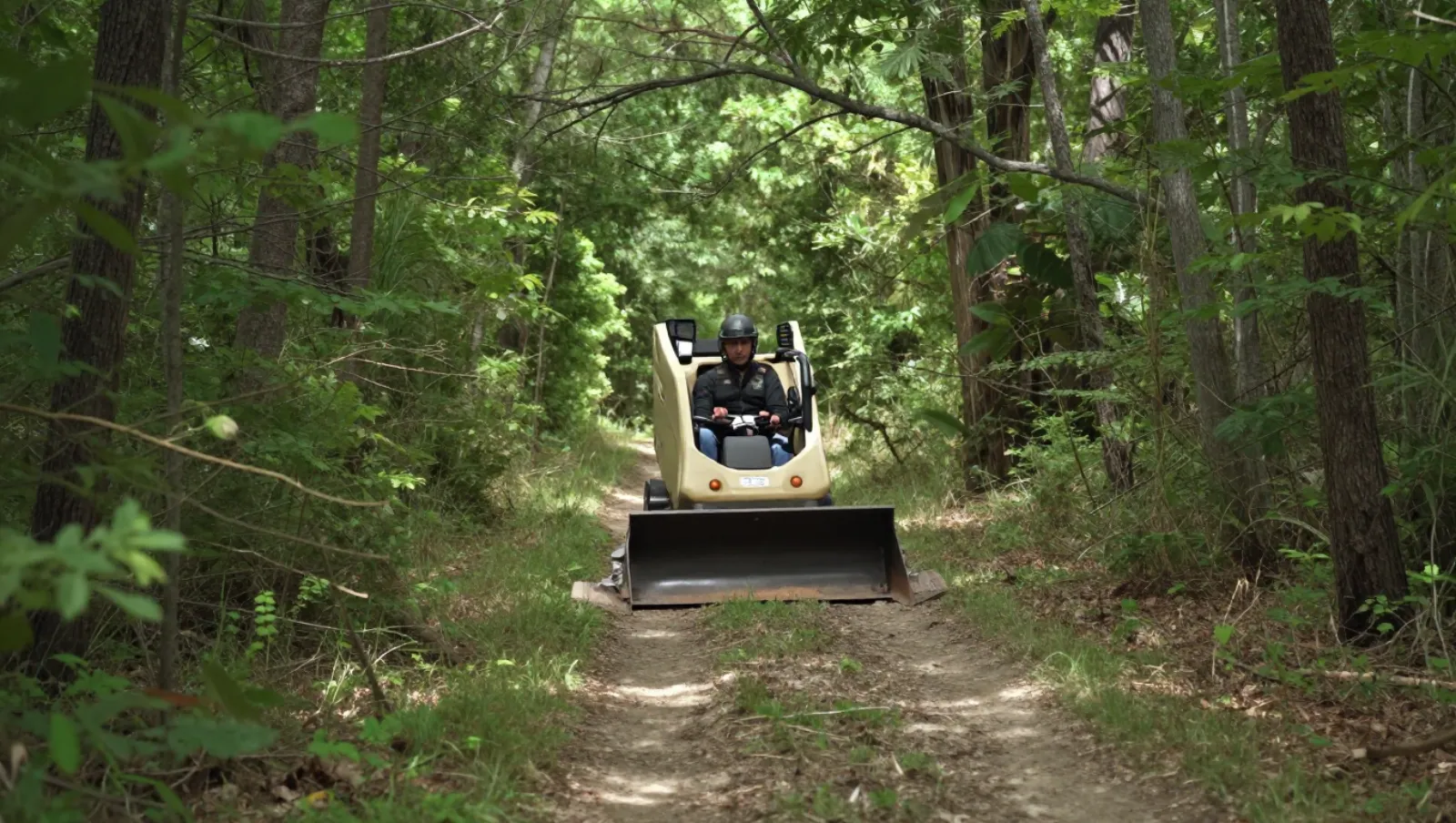 Arena and trail construction in Houston, Texas — Daniel Dean Land Clearing Driver operates a skid-steer loader along a forest dirt path for trail maintenance tasks — riding arena and trail construction in Houston, Texas