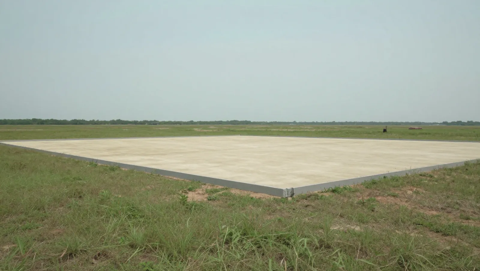 Dirt work in Sealy, Texas — completed work A large concrete foundation slab built on grassy terrain using construction machinery — dirt work and land grading in Sealy, Texas