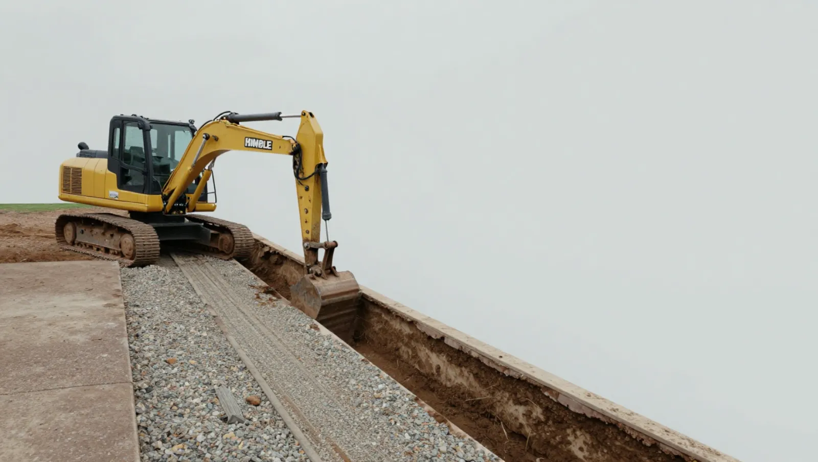 Drainage in Humble, Texas — Daniel Dean Land Clearing A yellow Kimble excavator loads soil into a trench on a construction site with gravel terrain — yard and property drainage in Humble, Texas