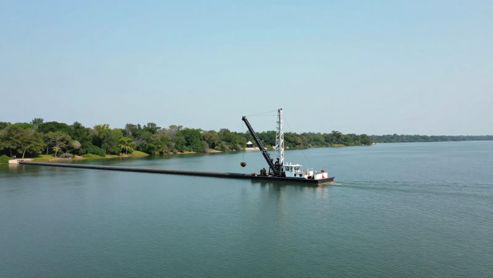 Pond services in Conroe, Texas — Daniel Dean Land Clearing Crane barge moves heavy objects across calm waters beside tree-lined shore — pond dredging and construction in Conroe, Texas