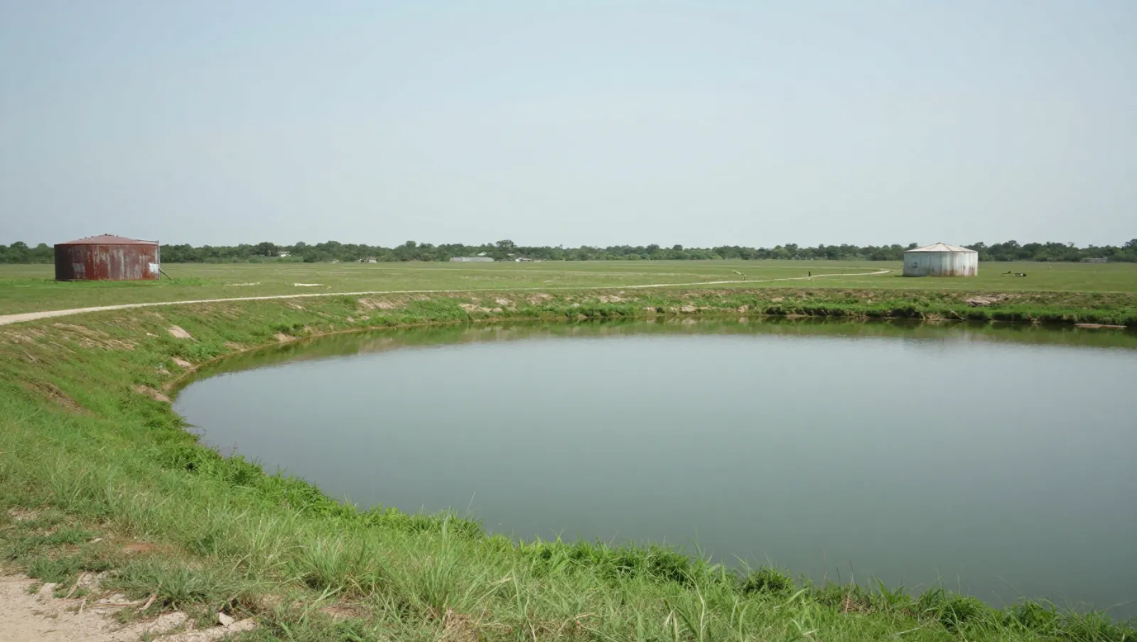 Pond services in Richmond, Texas — completed work Grain silos stand on flat grassland beside a pond for agricultural storage work — pond dredging and construction in Richmond, Texas