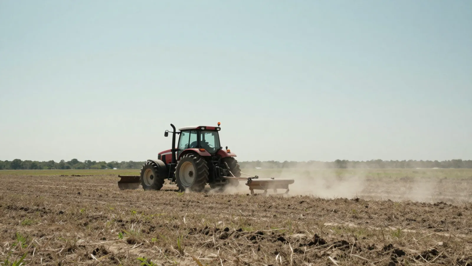 Land leveling in Houston, Texas — work underway A red tractor plows dry field soil, kicking up dust in an open farmland area — land leveling in Houston, Texas