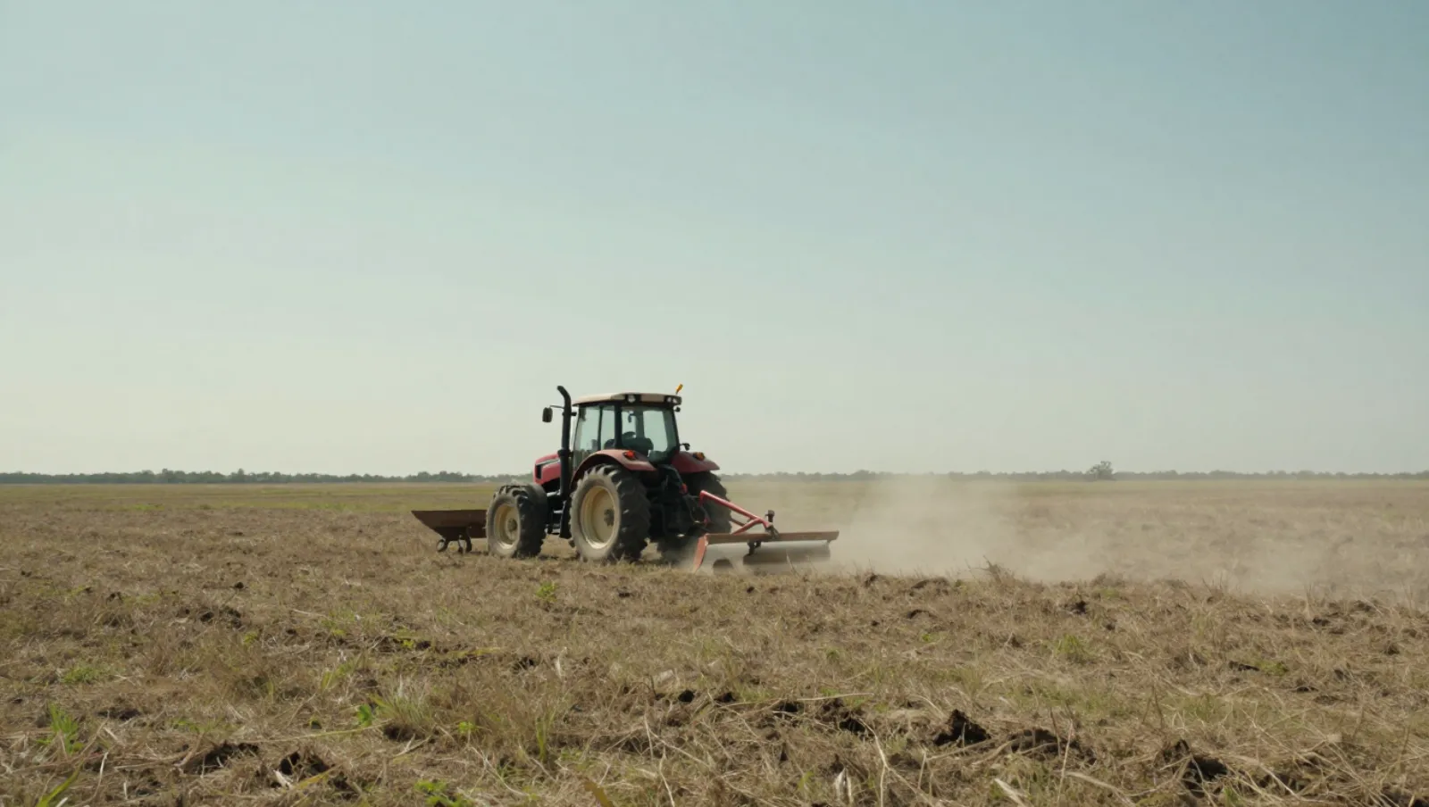 Land leveling in Sealy, Texas — work underway Red tractor plows dry brown grassy field, kicking up dust as it works — land leveling in Sealy, Texas