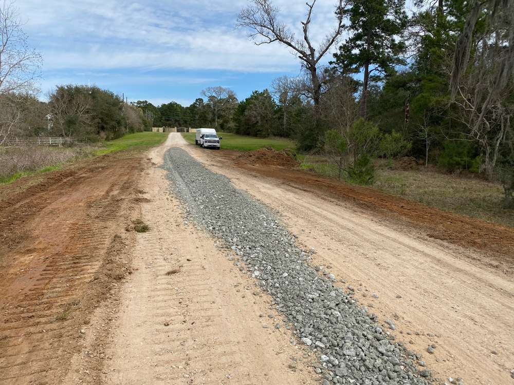 Fresh aggregate placed along the center of a long rural driveway before final grading and compaction